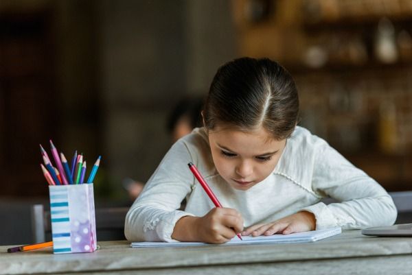 ittle child sitting at table and drawing in scrapbook at home